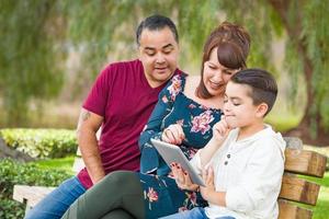 Kaukasisch moeder en spaans vader gebruik makend van computer tablet met gemengd ras zoon buitenshuis foto