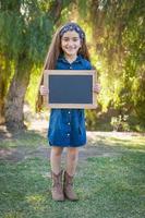 schattig jong gemengd ras meisje Holding blanco schoolbord buitenshuis foto