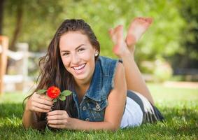 aantrekkelijk gemengd ras meisje portret houdende in gras buitenshuis met bloem. foto