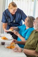 vrouw dokter of verpleegster portie senior volwassen paar boterhammen Bij tafel foto