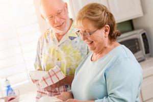 senior volwassen paar hebben pret het wassen gerechten samen binnen keuken van hun huis foto