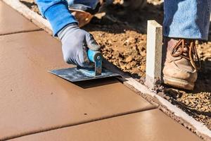 bouw arbeider gebruik makend van hand- groover Aan nat cement vormen omgaan in de omgeving van nieuw zwembad foto