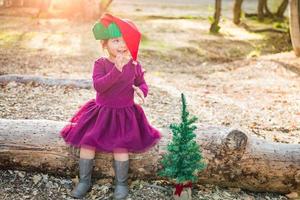 schattig gemengd ras jong baby meisje hebben pret met Kerstmis hoed en boom buitenshuis foto