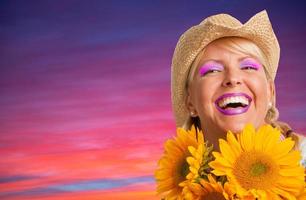 mooi lachend meisje vervelend cowboy hoed Holding geel zonnebloemen tegen Purper en roze zonsondergang foto