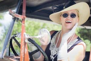 aantrekkelijk vrouw in jaren twintig kleding het rijden een antiek auto- foto