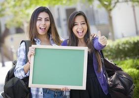 gemengd ras vrouw studenten met duimen omhoog Holding blanco schoolbord foto