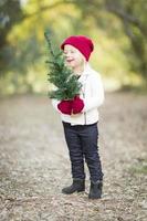 baby meisje in rood wanten en pet Holding klein Kerstmis boom foto