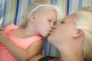 weinig meisje houdende Aan deken kusjes haar mama foto