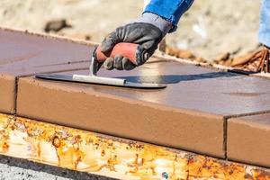 bouw arbeider gebruik makend van troffel Aan nat cement vormen omgaan in de omgeving van nieuw zwembad foto