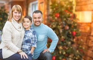 jong gemengd ras familie in voorkant van Kerstmis boom foto