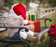 jong kind vervelend de kerstman hoed zittend met Kerstmis cadeaus buiten. foto