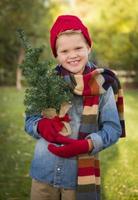 jong jongen vervelend vakantie kleding Holding klein Kerstmis boom buiten foto