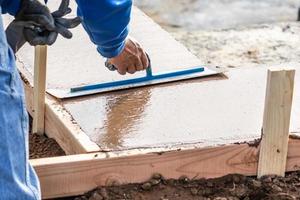 bouw arbeider gebruik makend van troffel Aan nat cement vormen omgaan in de omgeving van nieuw zwembad foto