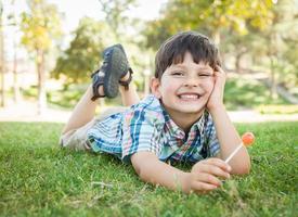 knap jong jongen genieten van zijn lolly buitenshuis Aan de gras. foto