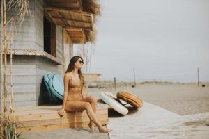 jong vrouw in bikini zittend Aan de strand Bij zomer dag foto