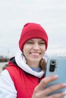 portret van jong vrouw in helder rood en wit warm sport kleren buitenshuis gebruik makend van smartphone foto