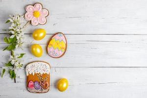 Pasen achtergrond met bloeiend appel boom tak, geel eieren, peperkoeken Aan wit houten tafel. foto