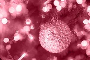 glas getextureerde Kerstmis bal hangende in Kerstmis boom met vakantie lichten in kleur 2023 viva magenta. foto