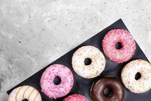 zwart omhulsel papier met gekleurde traditioneel donuts is aan het liegen diagonaal Aan grijs beton achtergrond met kopiëren ruimte. foto