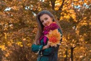 jong glimlachen meisje staat zijwaarts Aan de straat en houdt de droog bladeren met lijsterbes foto