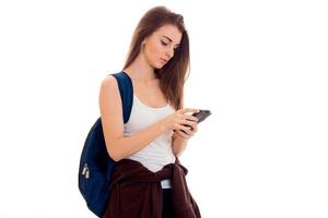 jong meisje in wit overhemd en met een aktentas Aan de terug looks in mobiel telefoon foto