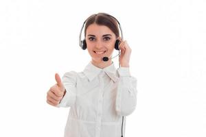 mooi jong brunette bedrijf vrouw met hoofdtelefoons en microfoon tonen duimen omhoog en glimlachen geïsoleerd Aan wit achtergrond foto