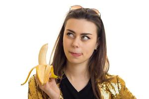 brunette vrouw in gouden jasje aan het eten een banaan foto