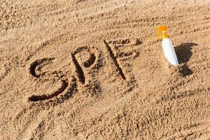 zon beschermen factor. spf woord geschreven Aan de zand en wit fles met zonnebrand room. huid zorg concept achtergrond foto
