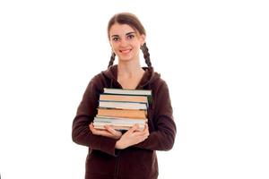 jong gelukkig brunette leerling meisje in bruin sport kleren met vlechten en boeken in haar handen glimlachen Aan camera geïsoleerd Aan wit achtergrond foto