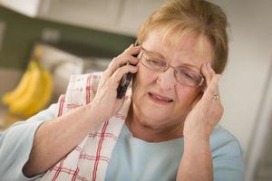 geschokt senior volwassen vrouw Aan cel telefoon in keuken foto