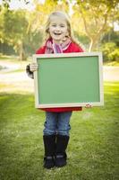 schattig meisje Holding een groen schoolbord vervelend winter jas buitenshuis foto