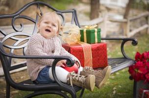 jong kleuter kind zittend Aan bank met Kerstmis cadeaus buiten foto