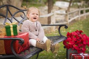 jong kleuter kind zittend Aan bank met Kerstmis cadeaus buiten foto