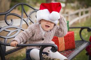 jong kind vervelend de kerstman hoed zittend met Kerstmis cadeaus buiten. foto