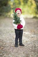 baby meisje in rood wanten en pet Holding klein Kerstmis boom foto