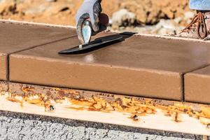 bouw arbeider gebruik makend van troffel Aan nat cement vormen omgaan in de omgeving van nieuw zwembad foto