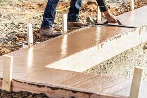bouw arbeider gebruik makend van hout troffel Aan nat cement vormen omgaan in de omgeving van nieuw zwembad foto