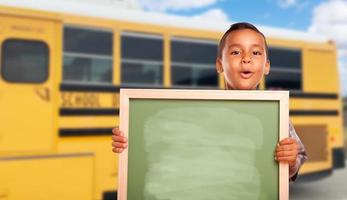 jong spaans jongen met blanco schoolbord in de buurt school- bus foto