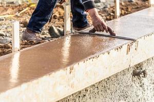 bouw arbeider gebruik makend van hout troffel Aan nat cement vormen omgaan in de omgeving van nieuw zwembad foto