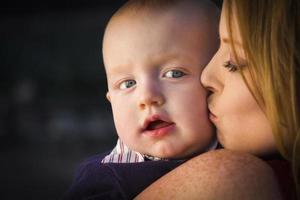 aanbiddelijk rood hoofd zuigeling jongen is gekust door zijn moeder foto