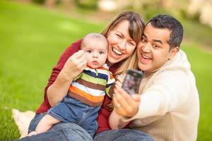 gelukkig gemengd ras ouders en baby jongen nemen zelf portretten Bij de park foto