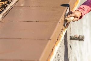 bouw arbeider gebruik makend van hout troffel Aan nat cement vormen omgaan in de omgeving van nieuw zwembad foto