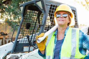 vrouw arbeider Holding technisch blauwdrukken in de buurt klein bulldozer Bij bouw plaats foto