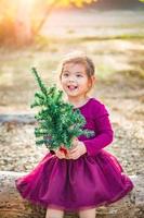 schattig gemengd ras jong baby meisje hebben pret met Kerstmis boom buitenshuis Aan log foto