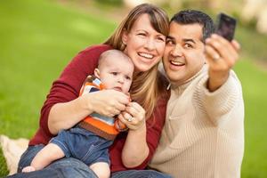 gelukkig gemengd ras ouders en baby jongen nemen zelf portretten Bij de park foto