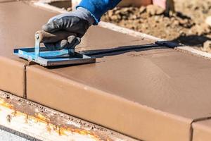 bouw arbeider gebruik makend van hand- groover Aan nat cement vormen omgaan in de omgeving van nieuw zwembad foto