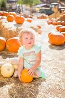 aanbiddelijk baby meisje hebben pret in een rustiek boerderij instelling Bij de pompoen lapje. foto