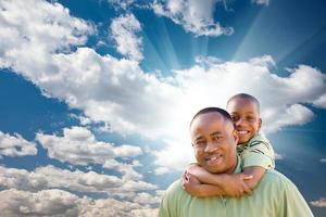 gelukkig Afrikaanse Amerikaans Mens met kind over- wolken en lucht foto