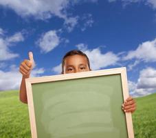 jongen met duimen omhoog in veld- Holding blanco krijt bord foto
