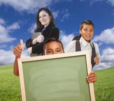 jong jongens met blanco krijt bord, leraar achter Aan gras foto